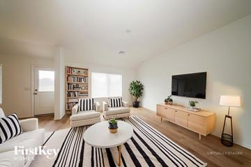 Tuttle house for rent - A living room with a white sofa, a black and white striped rug, a wooden coffee table, a flat screen TV, and a bookshelf with books and plants.