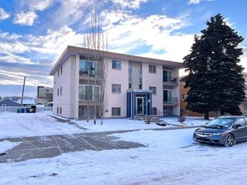 Calgary apartment for rent - A car is parked in front of a building with a tree to the right.