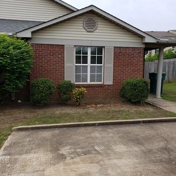 Tupelo apartment for rent - A small house with a window and a door surrounded by bushes and a driveway.
