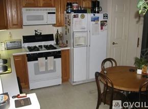 Gaithersburg house for rent - A kitchen with a white refrigerator, wooden cabinets, and a black stove top.