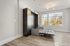 Chicago apartment for rent - A room with a wooden floor, a white wall, a brown wardrobe, a bed with a grey headboard, and a window with a view of trees and buildings outside.