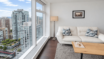 Vanvcouver apartment for rent - A living room with a white couch and a view of a cityscape through a large window.