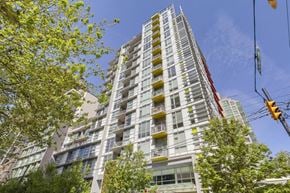 Vancouver apartment for rent - A tall building with many windows and balconies is surrounded by trees and has a clear blue sky in the background.