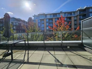 Vancouver apartment for rent - A balcony with a table and chairs overlooking a building and trees.