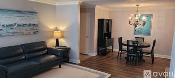 St. Simons Island condo for rent - A living room with a black leather couch, a wooden dining table with chairs, a chandelier, and a painting on the wall.