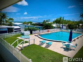 Key West apartment for rent - A pool with chairs and an umbrella is surrounded by a white fence.