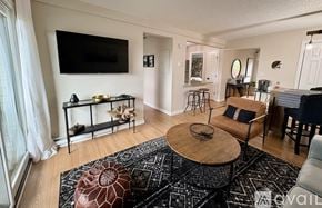 Laconia condo for rent - A living room with a black and white rug, a wooden coffee table, and a flat screen TV mounted on the wall.