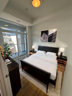Kitchener apartment for rent - A bedroom with a large bed and a window overlooking a city.