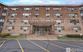 Ewing Township apartment for rent - A large brick building with a glass entrance and a parking lot in front.