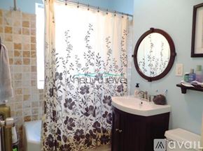 Boston apartment for rent - A bathroom with a floral shower curtain and a round mirror.