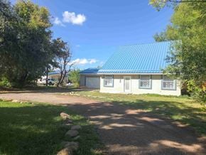 La Veta house for rent - A house with a blue roof is surrounded by greenery and a gravel path leads to the front door.