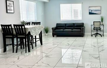 Los Angeles townhouse for rent - A living room with a black couch, a dining table with chairs, and a small potted plant.