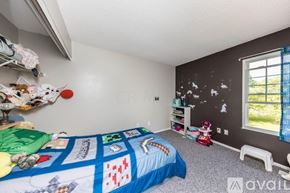 Hilliard condo for rent - A bedroom with a bed covered in a quilt, a window with a view of the outside, and a wall with a black and white pattern.