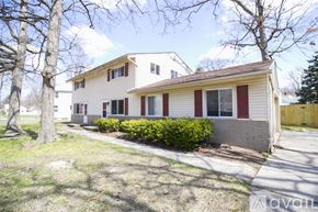 Toledo townhouse for rent - A house with a red trim and a grey roof is surrounded by a grassy area and trees.