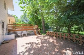 Cresskill house for rent - A patio with a wooden railing and a white chair is surrounded by trees.
