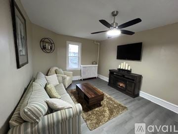 Ventnor City house for rent - A living room with a striped couch, a coffee table, and a television mounted on the wall.