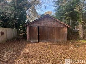 Hopewell house for rent - A small brown building with a closed door is surrounded by a fence and trees.