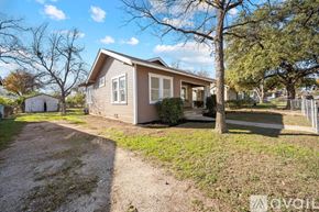 San Antonio house for rent - A house with a brown roof and a grey wall is surrounded by a gravel driveway and a grassy area.