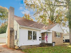 Akron apartment for rent - A small white house with a brown roof and a chimney is surrounded by trees with autumn leaves.