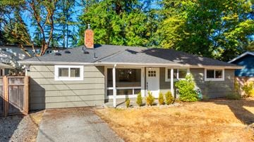 Seattle house for rent - A house with a grey exterior and a white door is surrounded by trees.
