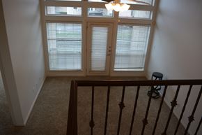 Austin apartment for rent - A room with a carpeted floor, a window with blinds, a chandelier, and a staircase with a railing.