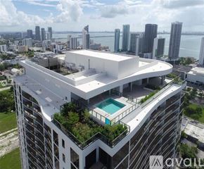 Miami condo for rent - A modern building with a pool on the top floor overlooks a cityscape.