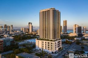 Miami condo for rent - A tall white building with balconies is the focal point of a cityscape.