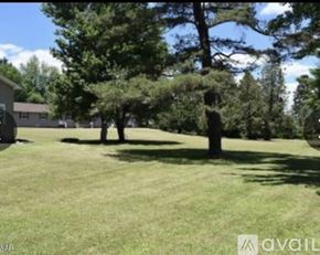 Honesdale townhouse for rent - A grassy field with trees and a house in the background.