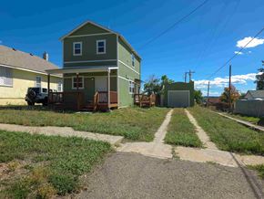 Walsenburg house for rent - A green house with a white door and windows is surrounded by a grassy area and a dirt path.