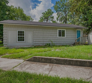 Jacksonville house for rent - A small house with a blue door and a window is surrounded by grass and trees.