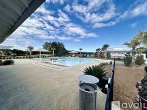 Hardeeville house for rent - A large outdoor swimming pool surrounded by a concrete patio and a metal trash can.