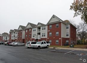 Memphis apartment for rent - A white car is parked in a parking lot in front of a red brick apartment building.