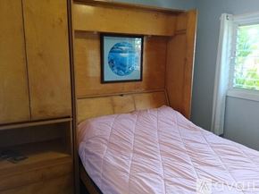 Kapaa apartment for rent - A bed with a pink comforter sits in a room with a wooden headboard and a picture of a globe on the wall.