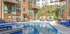 Dallas apartment for rent - A large swimming pool surrounded by lounge chairs and umbrellas in a modern building.