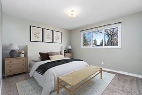 Edmonton apartment for rent - A bedroom with a bed, nightstand, and a window with a view of trees.
