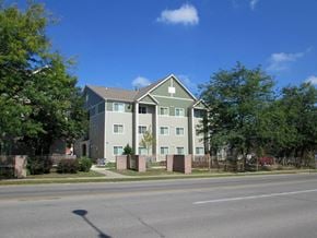 Des Moines apartment for rent - A grey building with a green roof is surrounded by trees.