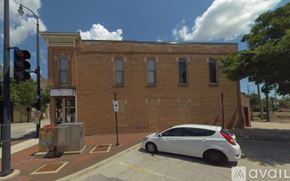 Dekalb apartment for rent - A white car is parked on the side of a street in front of a brick building.