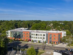 Detroit apartment for rent - A multi-story building with a red and white facade is surrounded by trees.