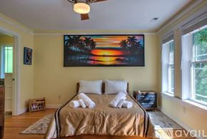 Asheville house for rent - A bedroom with a bed, a ceiling fan, and a painting of a sunset on the wall.