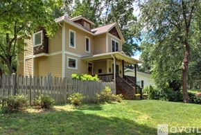 Asheville house for rent - A house with a yellow exterior and a brown roof is surrounded by a wooden fence and greenery.