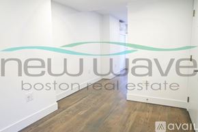 Boston apartment for rent - A room with wooden flooring and white walls, with a logo that reads "new wave boston real estate available".