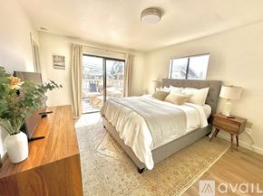 Oakland apartment for rent - A bedroom with a large bed and a wooden table with a vase of flowers on it.