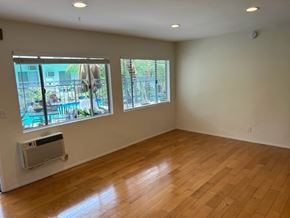 West Hollywood apartment for rent - A room with wooden floors and two windows overlooking a pool.