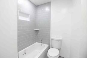West Springfield house for rent - A white toilet sits next to a white bathtub in a bathroom with grey tiled walls.
