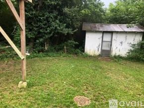 North Little Rock house for rent - A small white shed sits in a grassy area with trees in the background.