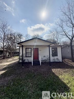 San Antonio house for rent - A small white house with a red door is situated in a grassy area with trees in the background.