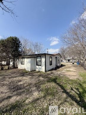 San Antonio house for rent - A small white house with a brown roof is surrounded by a grassy area and leafless trees.