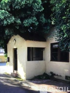 Los Angeles townhouse for rent - A small white house with a black door and windows is surrounded by trees.