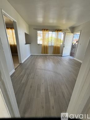 Los Angeles apartment for rent - A spacious room with wooden flooring and a window with yellow curtains.