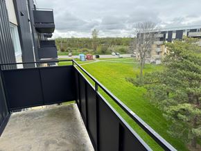 Amherstview apartment for rent - A balcony with a black railing overlooks a grassy area with trees and a building in the distance.